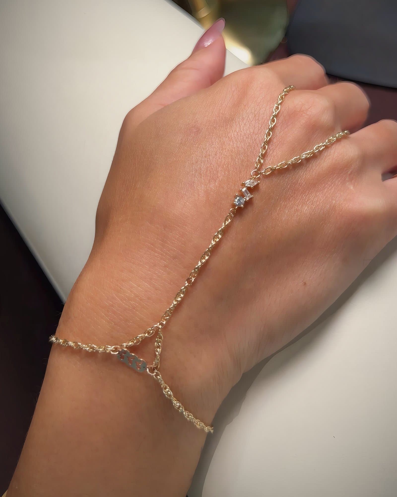 A Bond & Fifth gold hand chain with small crystal accents, worn on the back of a hand