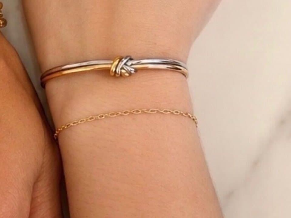 A fine gold-filled chain bracelet beside a knot bangle on a wrist, on marble